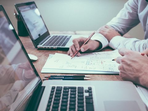 Zwei Personen am Holztisch mit Laptops skizzieren Bildschirmentwürfe auf Papier