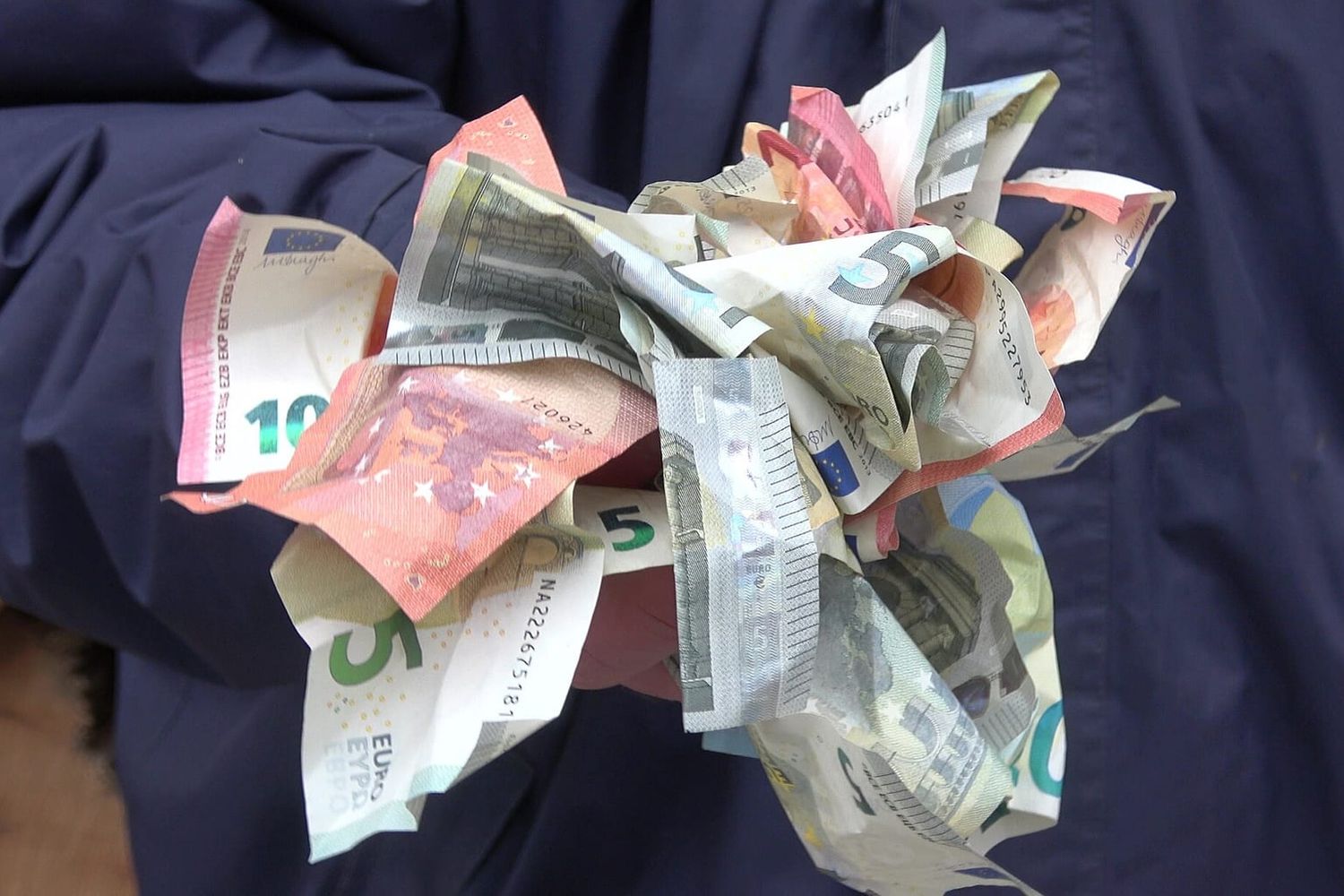 Zerknüllte Euro-Banknoten in zwei Händen vor einer dunkelblauen Jacke
