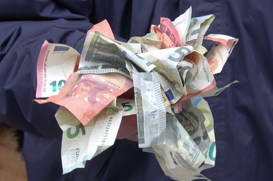 Zerknüllte Euro-Banknoten in zwei Händen vor einer dunkelblauen Jacke