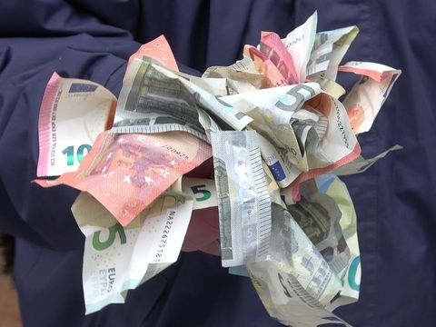 Zerknüllte Euro-Banknoten in zwei Händen vor einer dunkelblauen Jacke