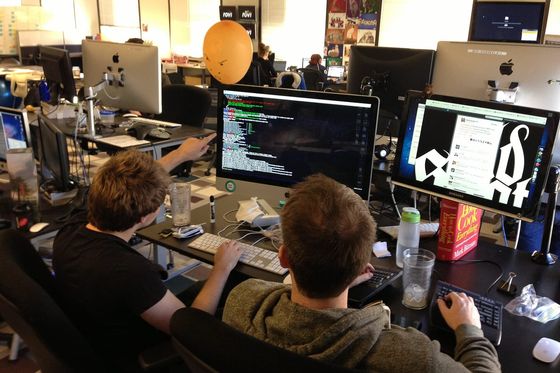 Zwei Entwickler von hinten vor Monitoren, einer zeigt auf Code im Terminal