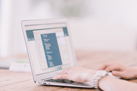 Hände tippen auf einem Laptop, auf dessen Bildschirm ein Code-Editor geöffnet ist