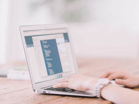 Hände tippen auf einem Laptop, auf dessen Bildschirm ein Code-Editor geöffnet ist