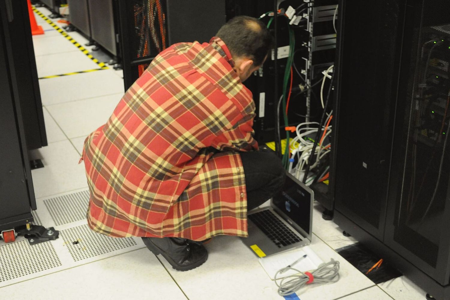 Techniker hockt mit Laptop vor einem geöffneten Serverschrank im Rechenzentrum