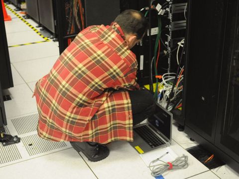 Techniker hockt mit Laptop vor einem geöffneten Serverschrank im Rechenzentrum