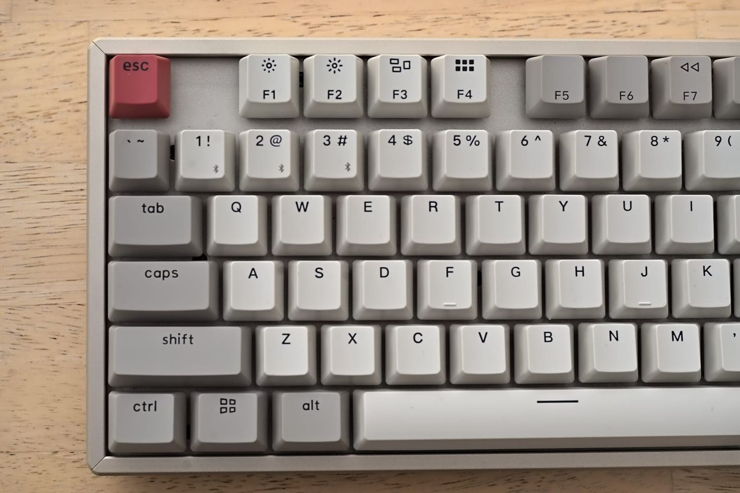 Helle mechanische Tastatur mit roter Escape-Taste auf einem Holztisch