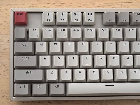 Helle mechanische Tastatur mit roter Escape-Taste auf einem Holztisch